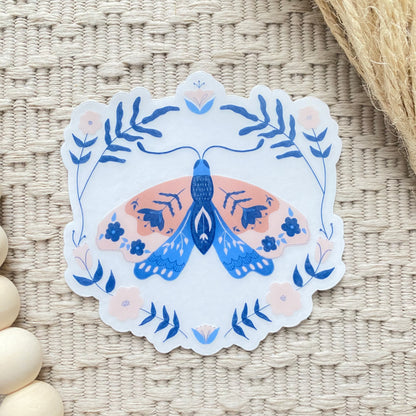 Decorative sticker with a floral blue and pink moth design on a woven surface
