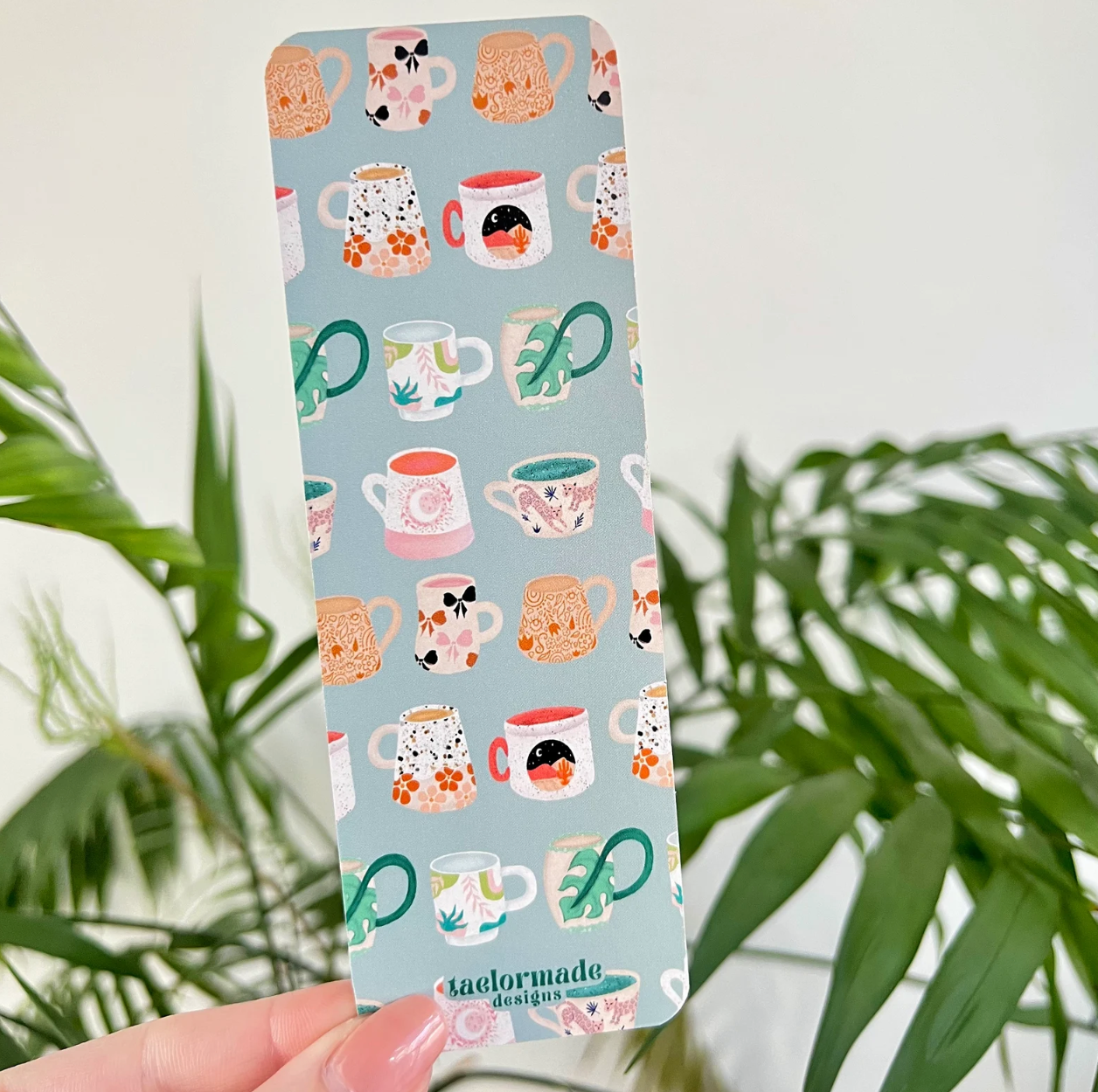 Bookmark with mug pattern held by a hand against a plant background