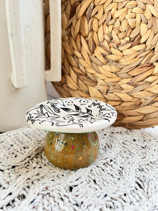 Decorative ceramic mushroom box with black floral design on a textured surface
