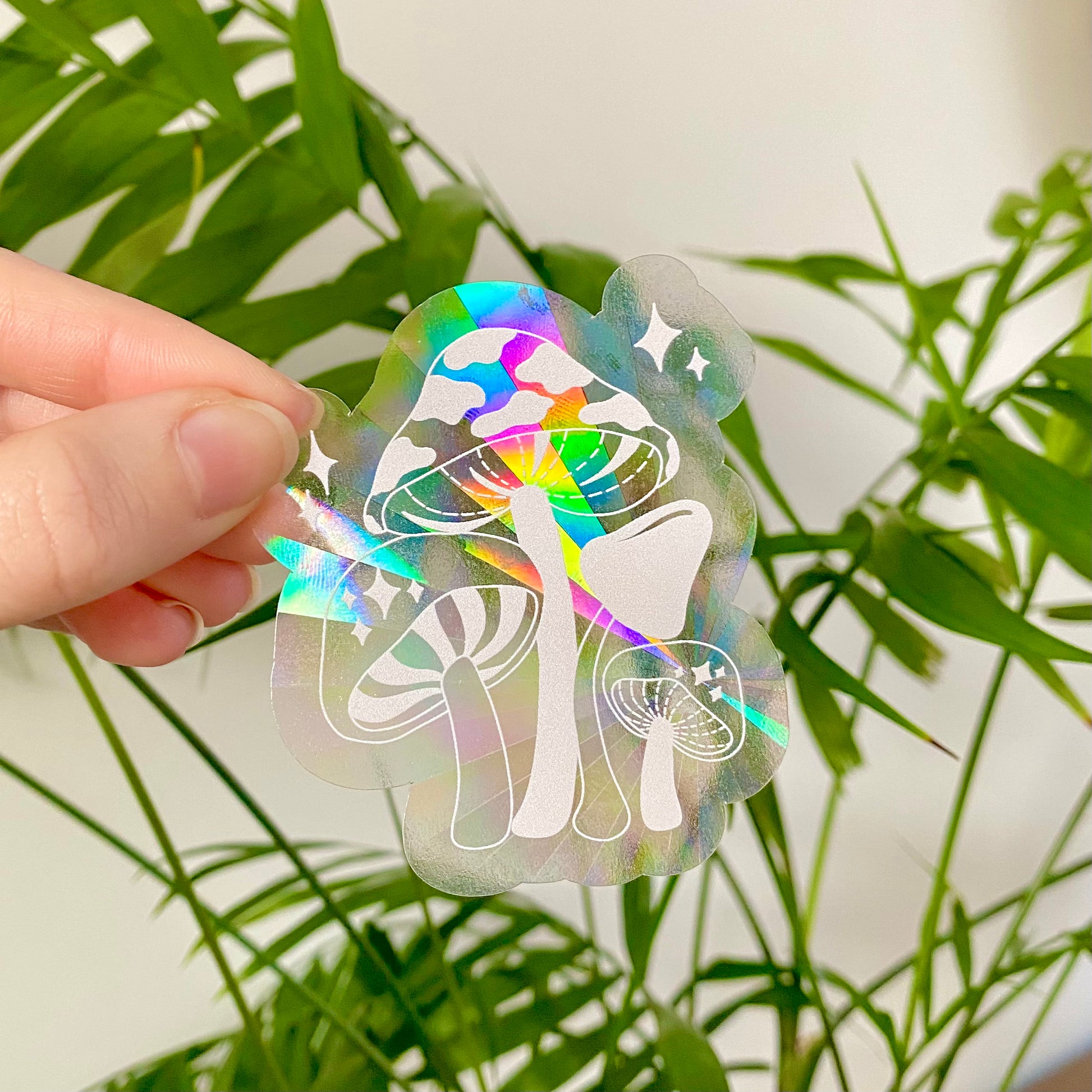 Holographic sticker with a mushroom design held by a hand against a plant background