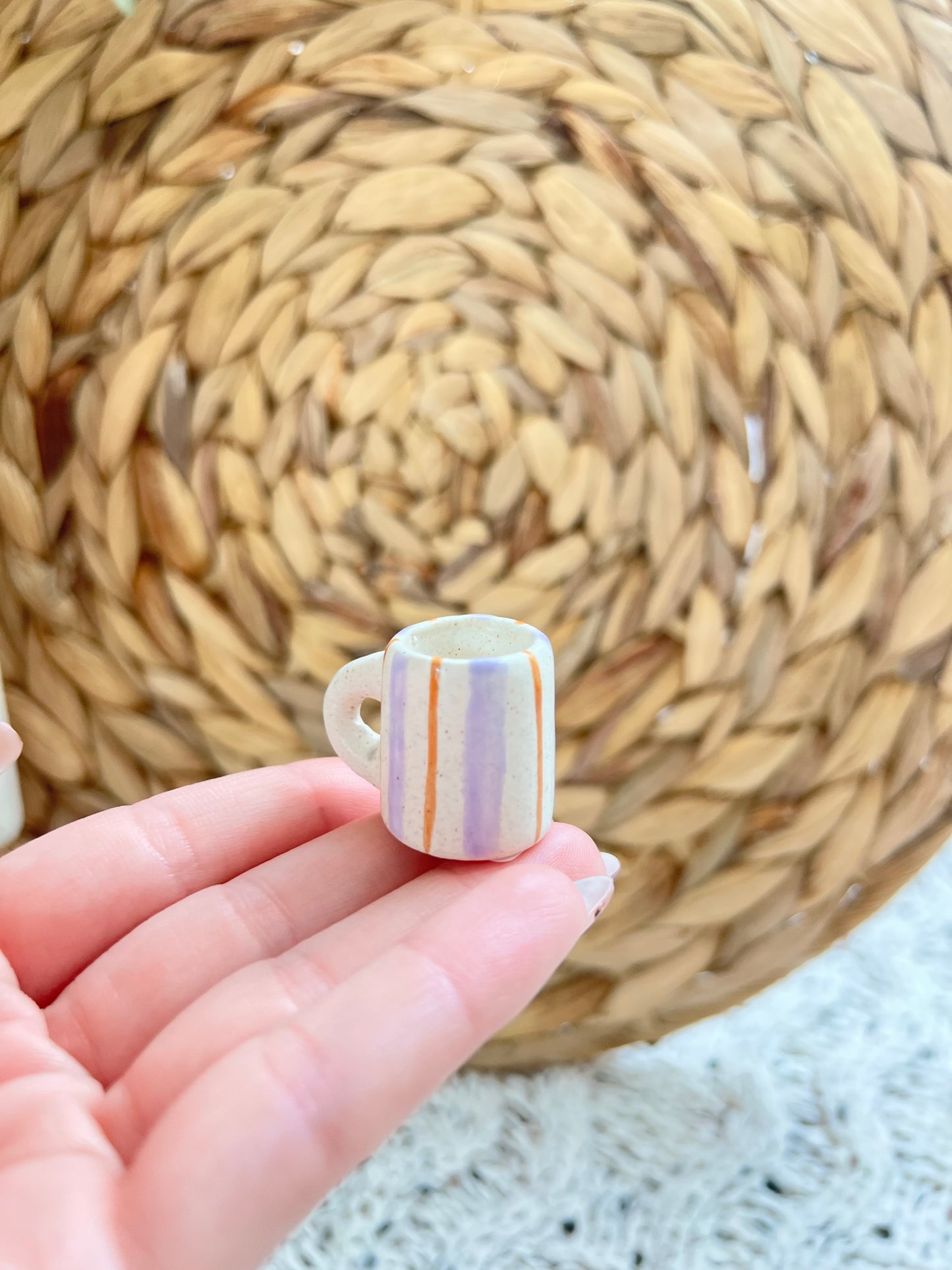 Small ceramic cup with colorful stripes held in a hand against a woven mat background