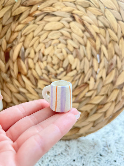 Small ceramic cup with colorful stripes held in a hand against a woven mat background