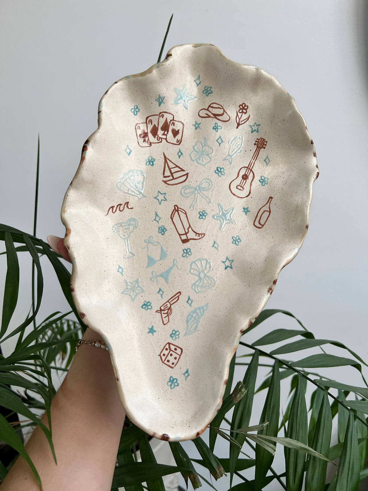 Decorative ceramic plate with illustrations held by a person against a plant background