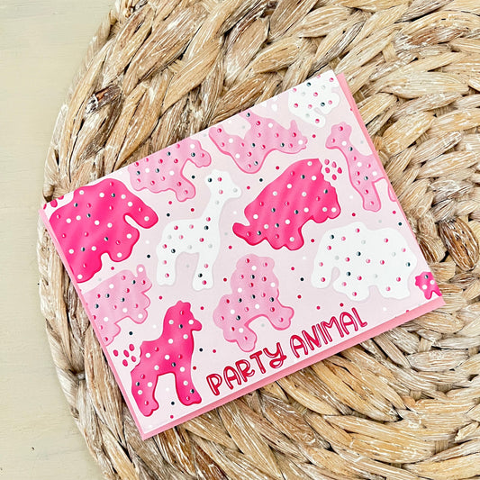 Pink card with frosted animal cracker design and 'Party Animal' text on a woven surface