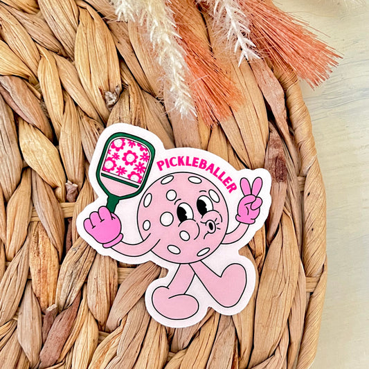 Sticker of a pink cartoon character holding a pickleball paddle on a woven surface