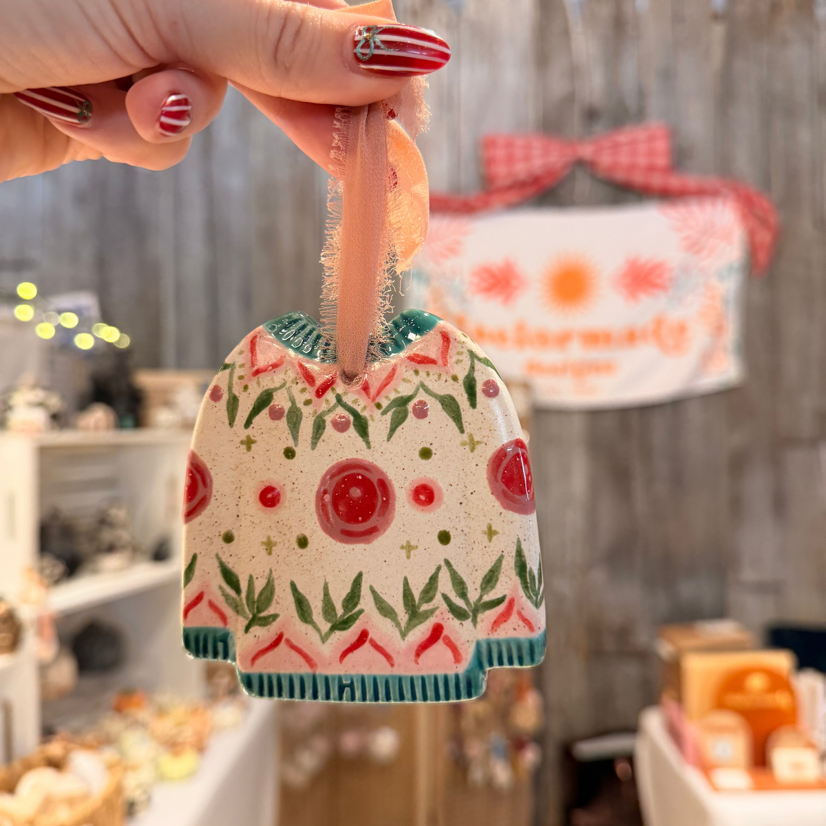 Decorative ceramic sweater ornament with floral pattern held by a hand in a store setting.