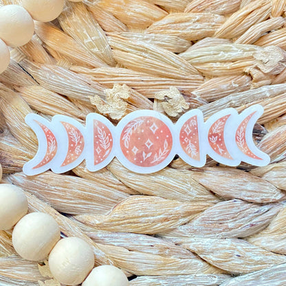 Sticker of pink moon phases on a woven surface with wooden beads