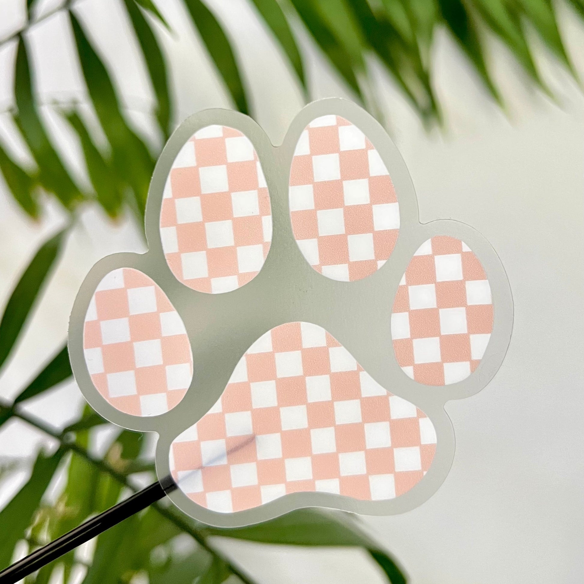 Checkered pink paw print design on a clear background with green leaves in the foreground