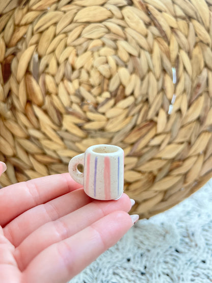 Small ceramic cup with colorful stripes held in a hand against a woven mat background
