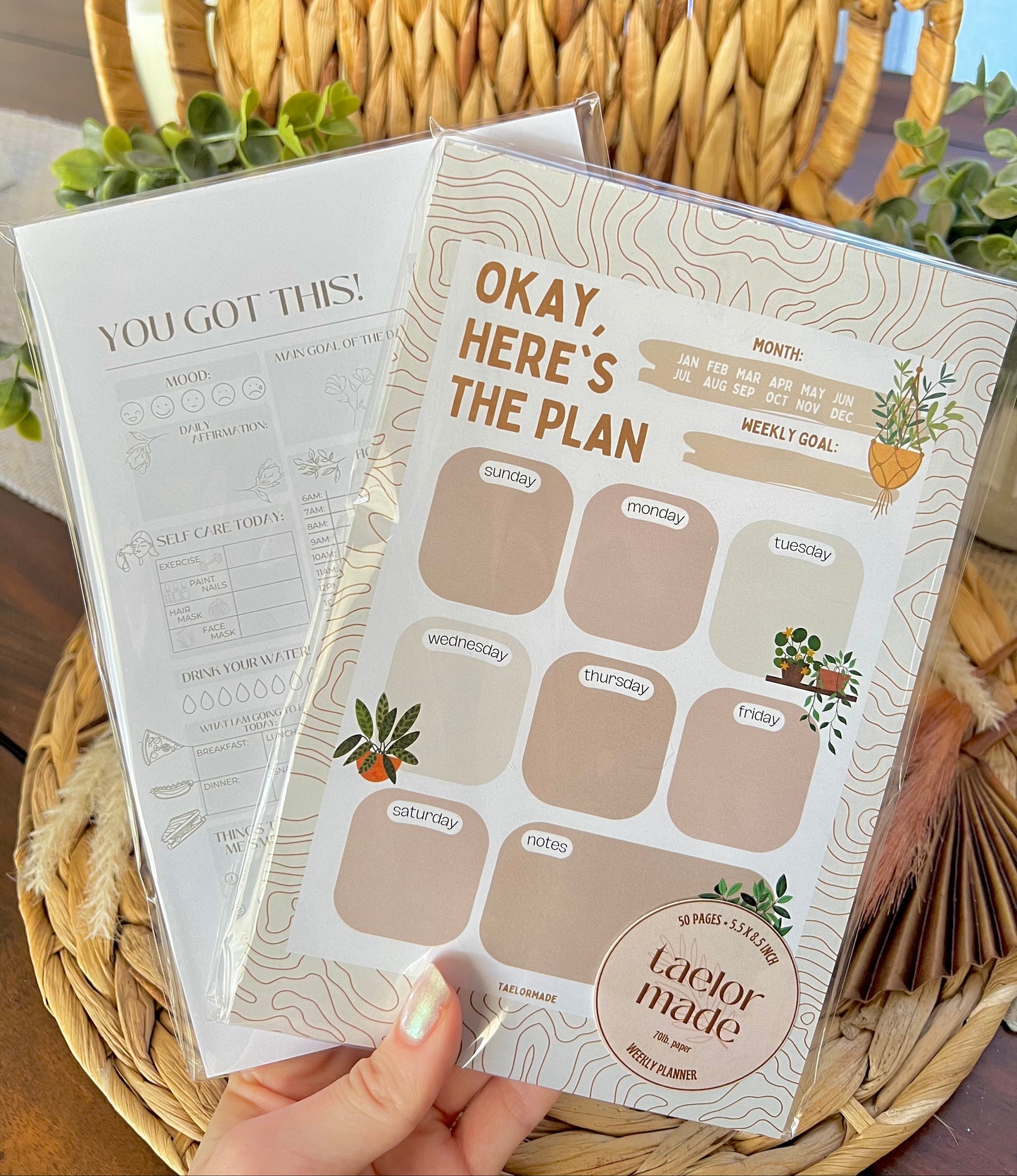 Two planner notepads held by a hand on a woven surface