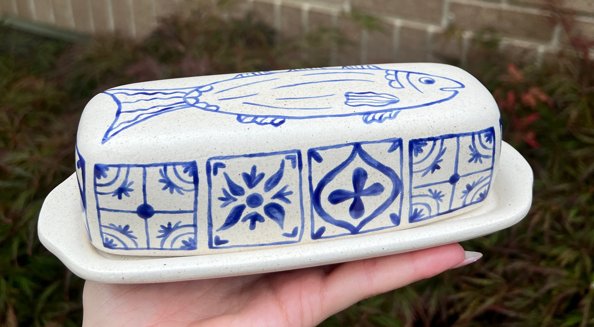 Butter dish with blue fish and geometric patterns held in front of a brick wall.