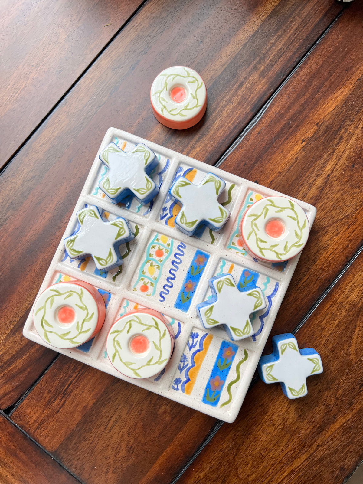 Set of ceramic tictactoe game with colorful designs on a wooden surface