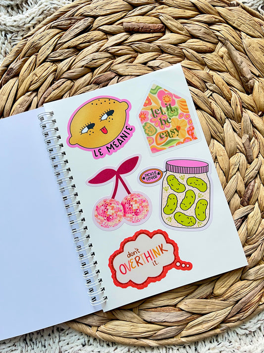 Sticker sheet with colorful designs on a notebook against a woven mat background