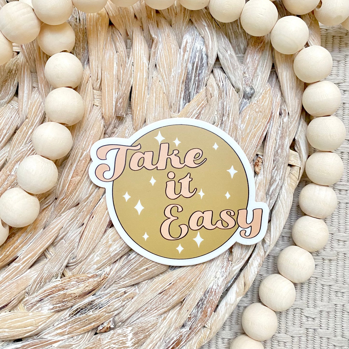 Sticker with 'Take it Easy' text on a woven background with beads