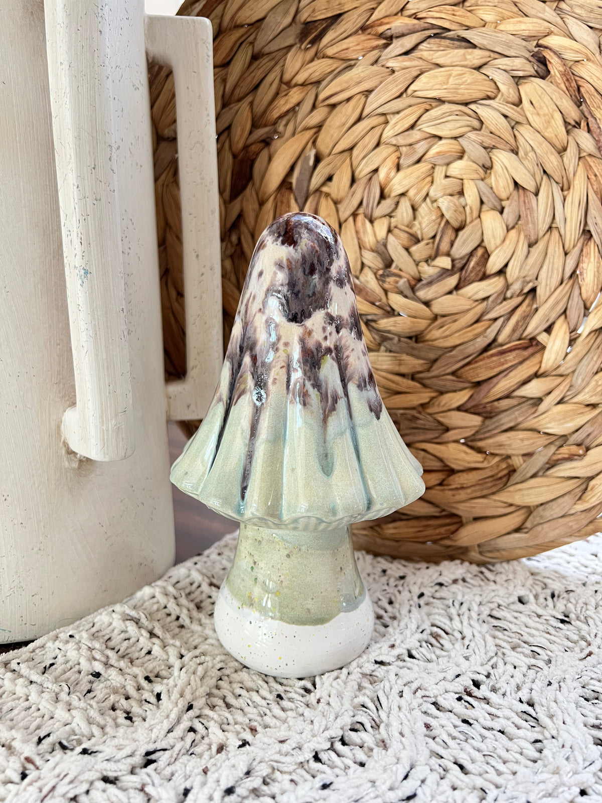 Decorative ceramic mushroom-shaped object on a textured surface with a woven basket in the background