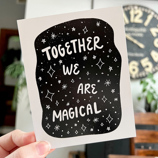 Card with 'Together We Are Magical' text over an illustration of stars and space held by a hand in a casual setting.