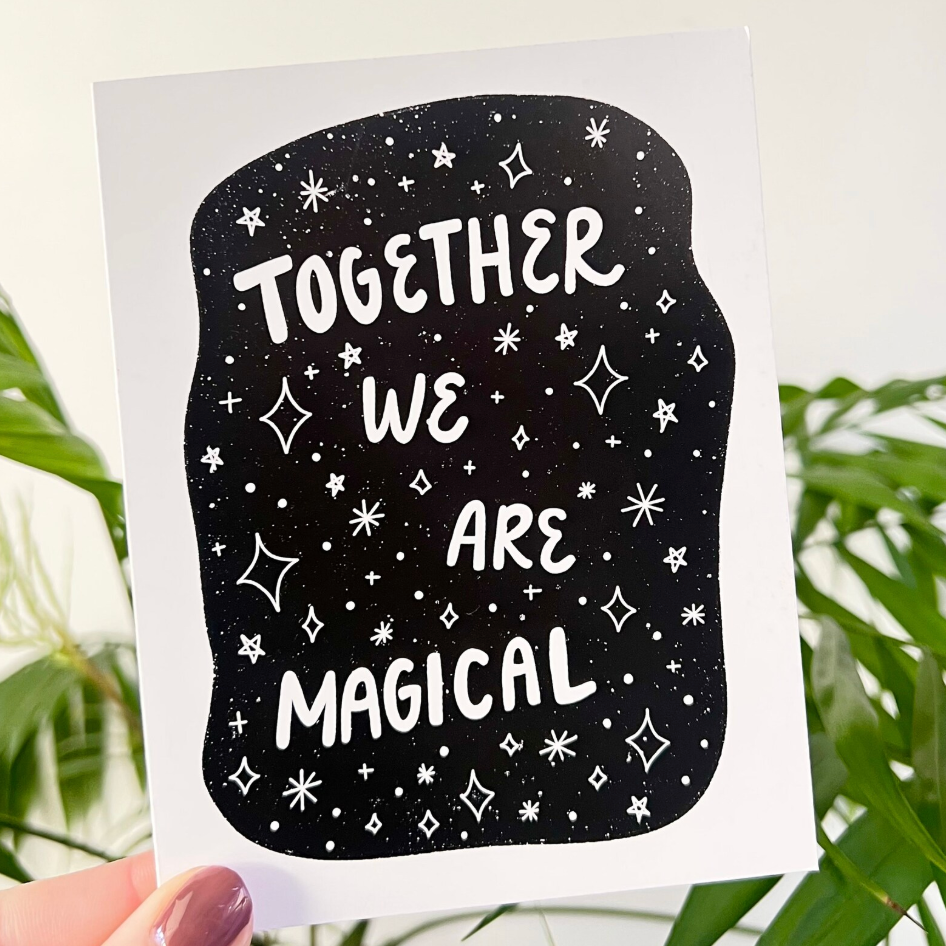 Card with 'Together We Are Magical' text on a black background with white stars held by a hand with greenery in the background