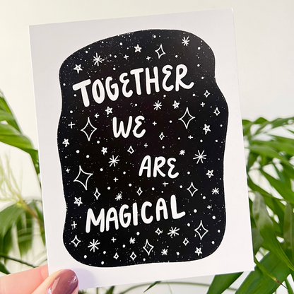 Card with 'Together We Are Magical' text on a black background with white stars held by a hand with greenery in the background