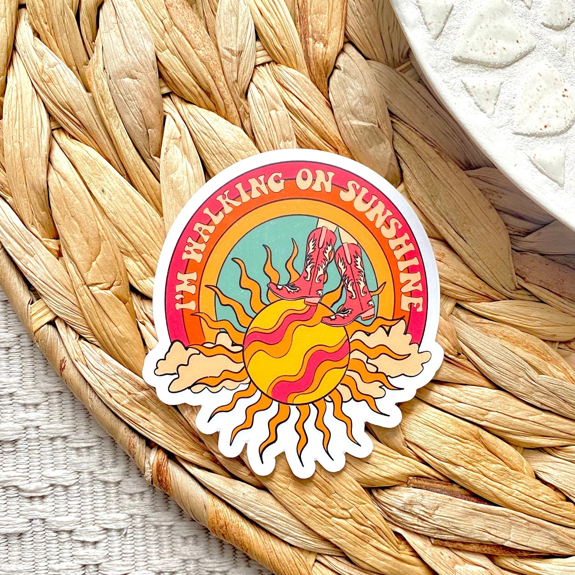 Sticker with a colorful design of a sun and text 'I'm Walking on Sunshine' on a woven mat.
