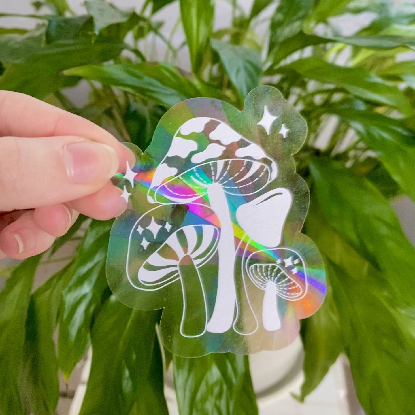 Mushroom suncatcher sticker refracting light and making rainbows in front of green plant